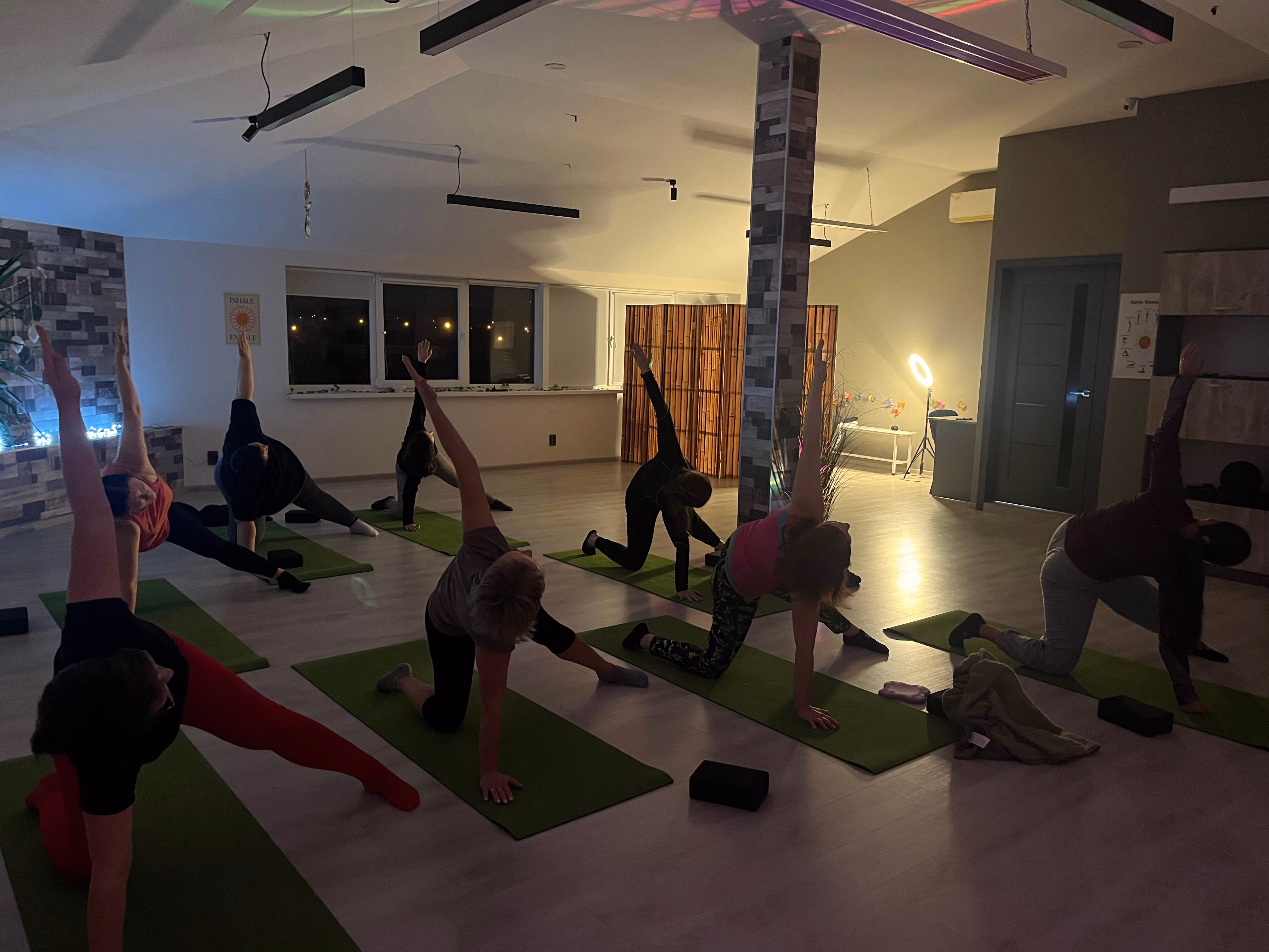 Велика група на занятті йогою, бічні нахили у вечірньому залі